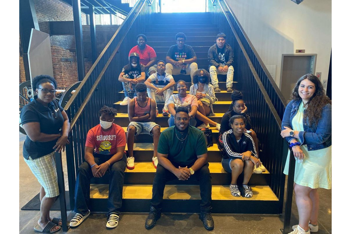 a group of mostly Black youth sitting on the steps of a stair.