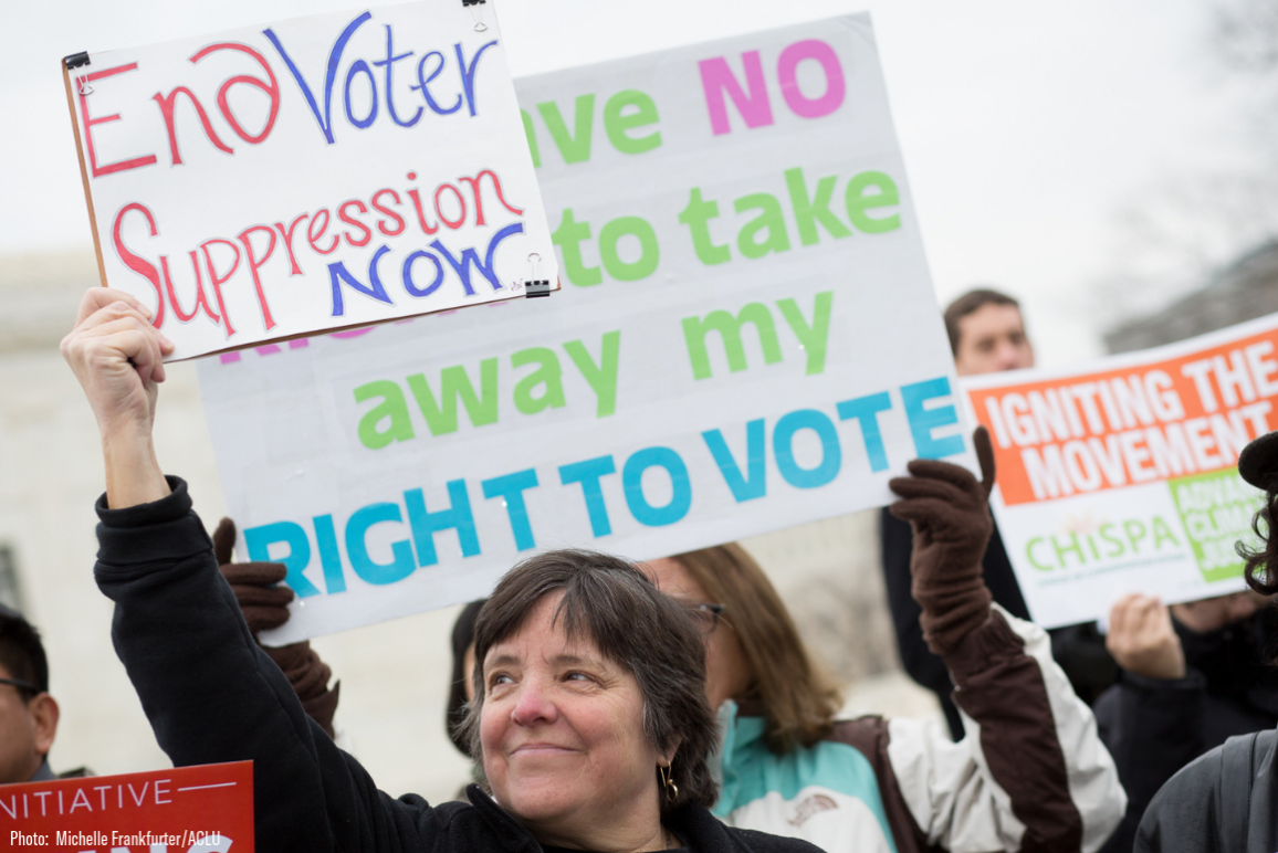 A white woman holding a sign that says "End Voter Suppression Now"