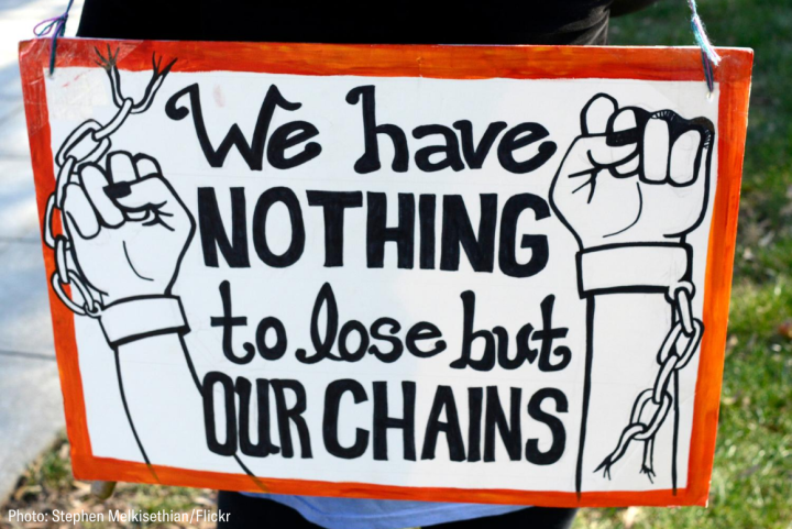 a white sign with red frame with two arms breaking away from a chain, text reads "we have nothing to lose but our chains"