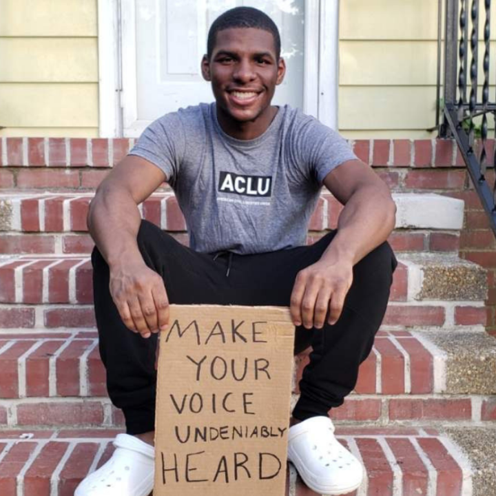 a photo of our intern Alton Coston sitting on the steps in front of his house, holding a cardboard sign that says "make your voice undeniably heard"