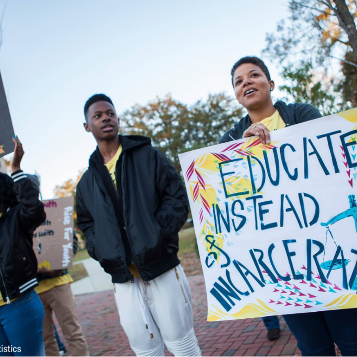 a black woman holding a sign that says "educate instead of incarcerate"