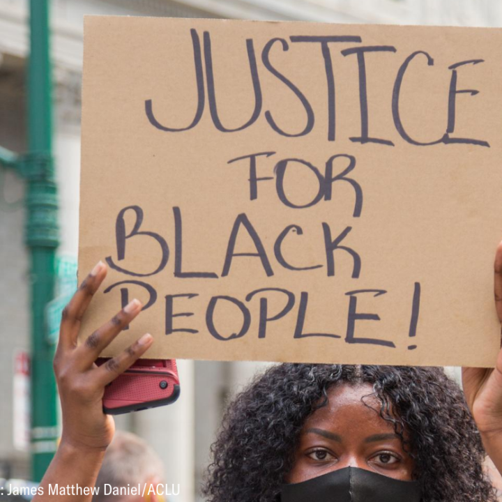 a black woman holding a cardboard sign that says "justice for black people!"